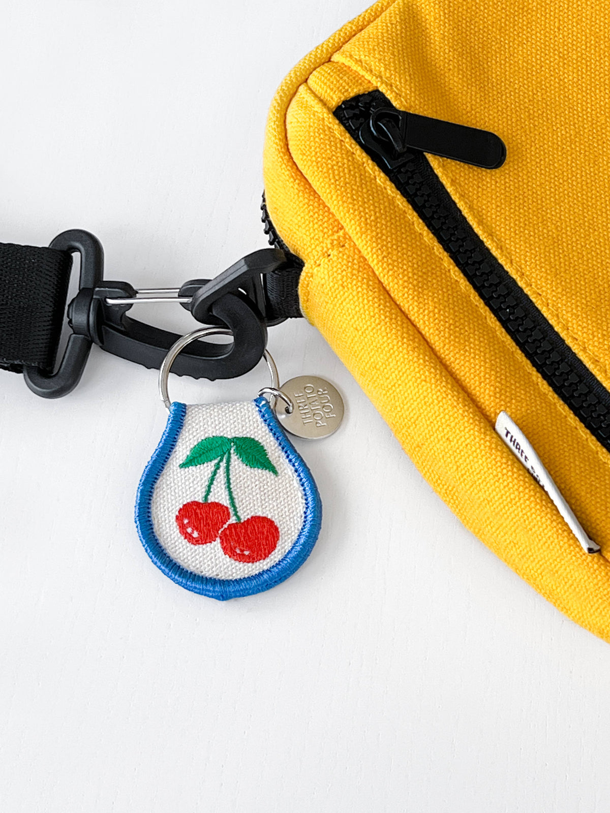 Yellow bag with a keychain featuring cherries on a white background