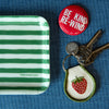 Green and white striped tray with a red button, keys, and a strawberry keychain on a blue background