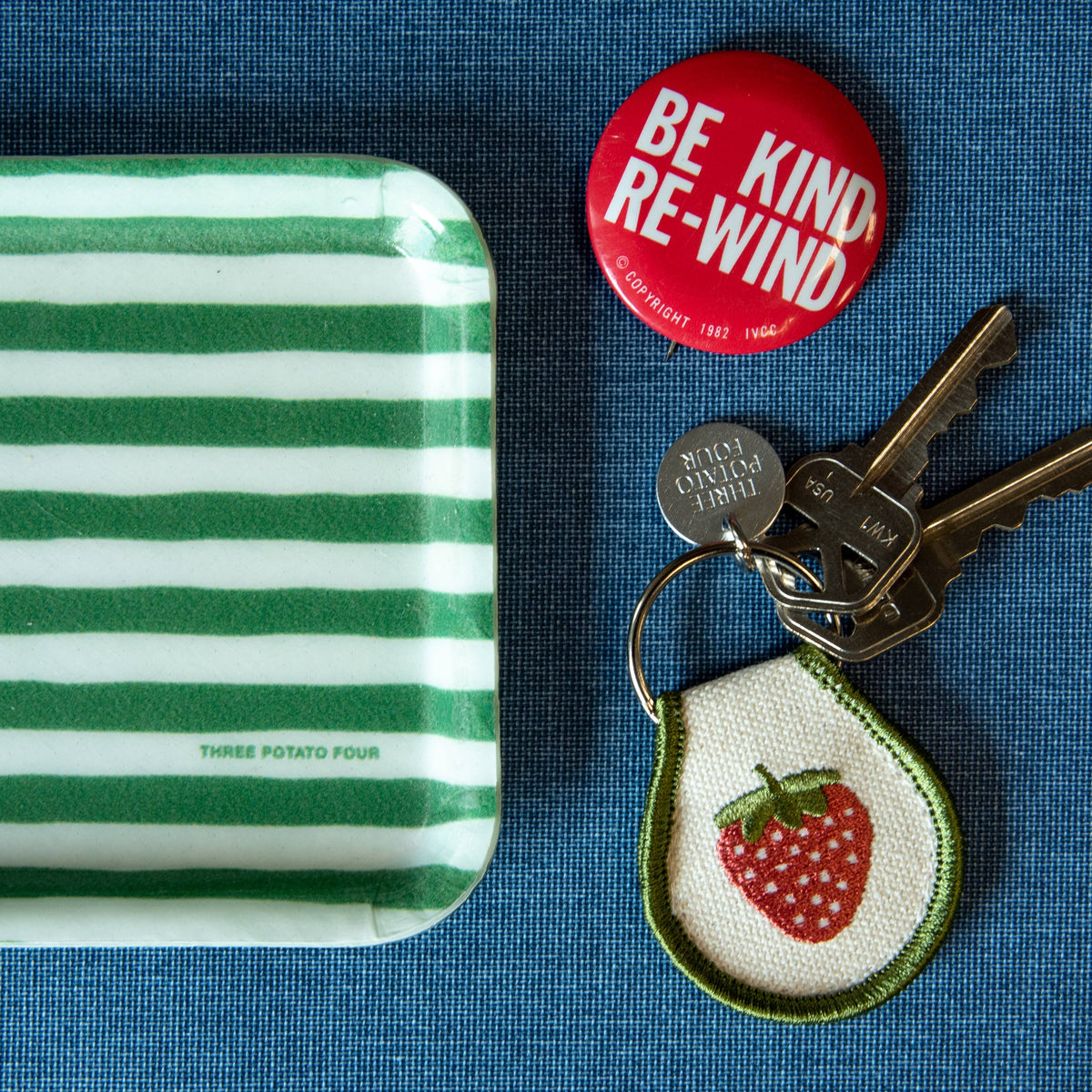 Green and white striped tray with a red button, keys, and a strawberry keychain on a blue background