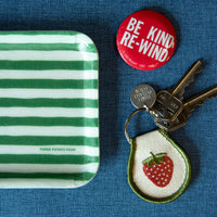 Green and white striped tray with a red button, keys, and a strawberry keychain on a blue background