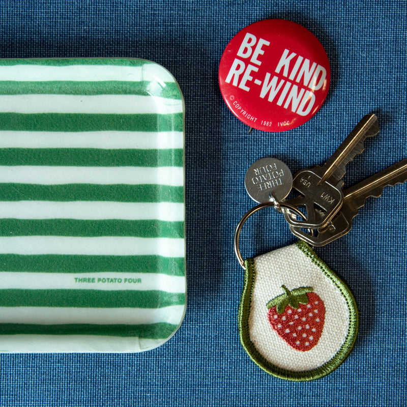 Green and white striped tray with a red button, keys, and a strawberry keychain on a blue background