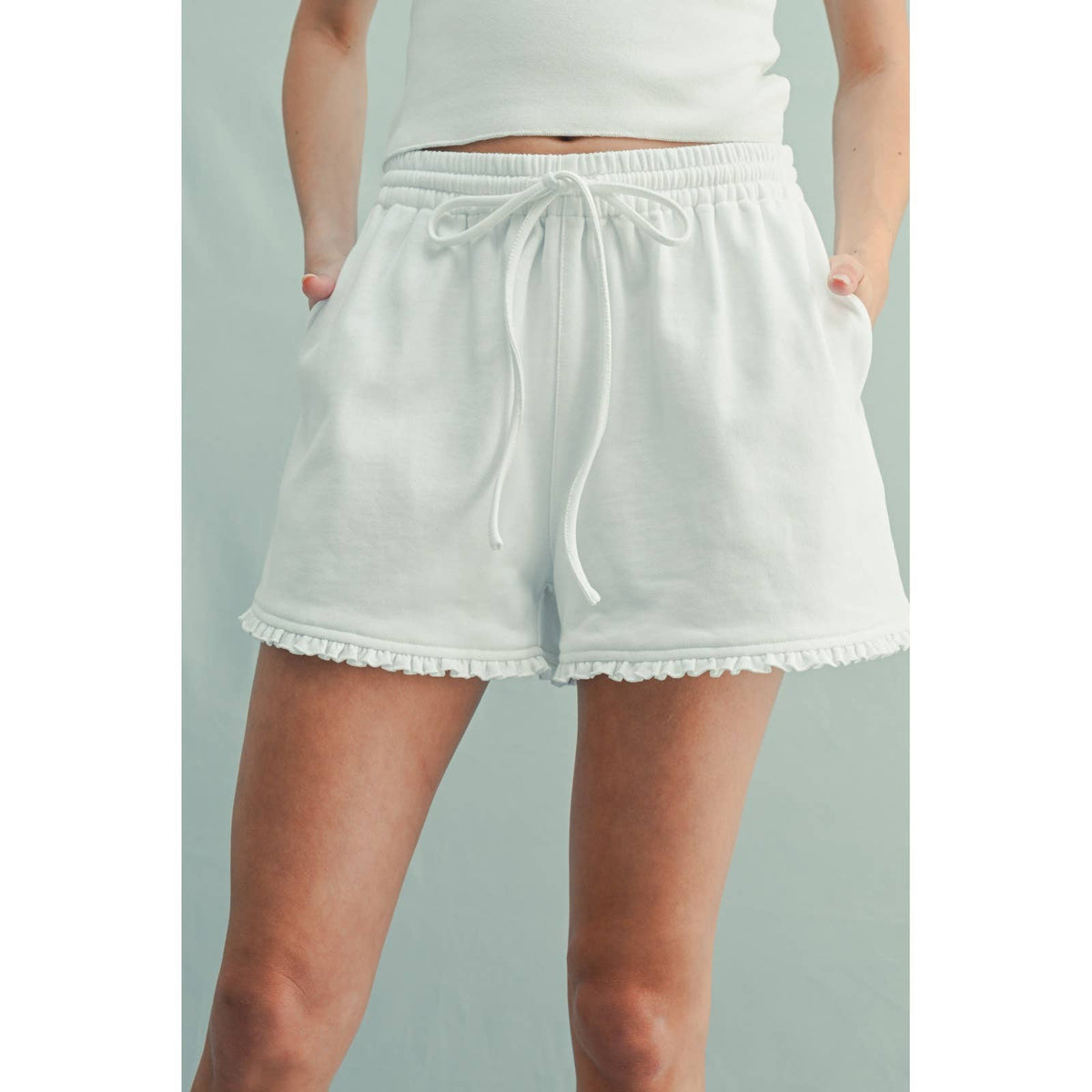 White shorts with lace trim worn by a person on a light gray background