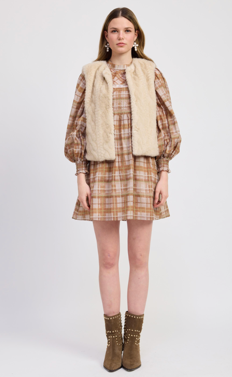 Woman wearing a plaid dress with a beige vest and brown boots on a white background