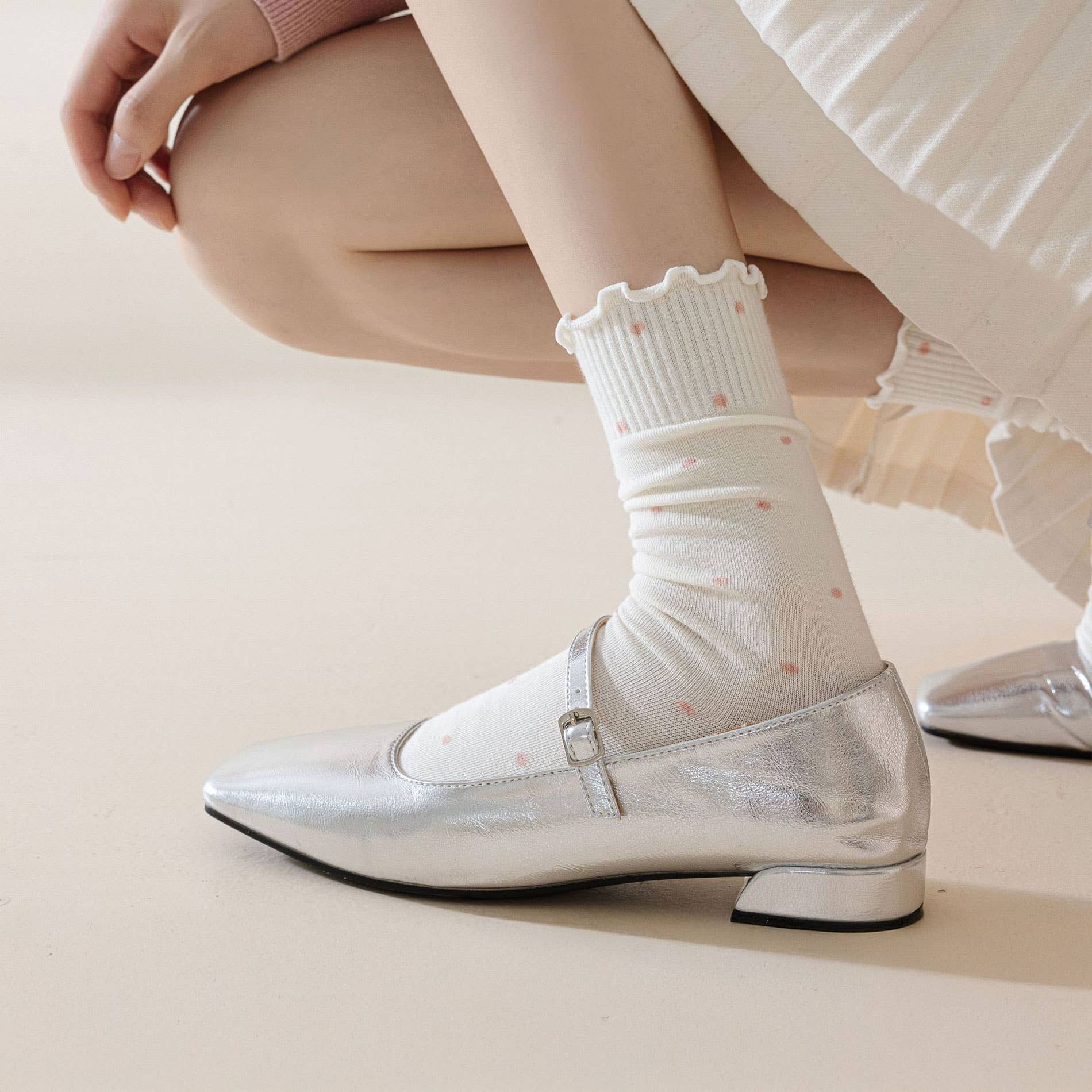Silver loafers worn with white socks on a neutral background