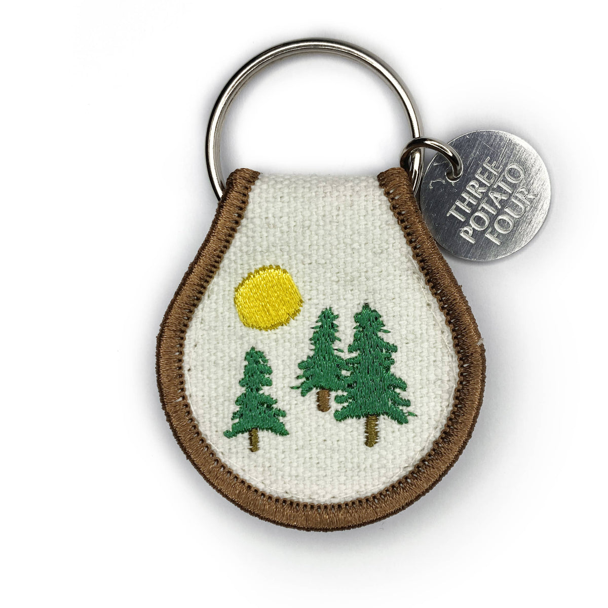Keychain with embroidered design of trees and sun, featuring a 'Three Potato Four' tag.