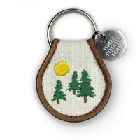 Keychain with embroidered design of trees and sun, featuring a 'Three Potato Four' tag.