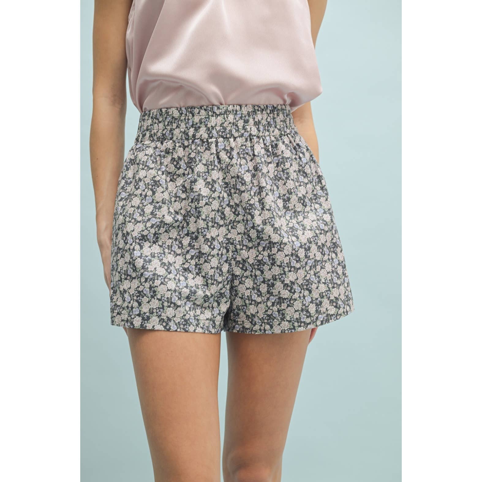 Person wearing floral shorts and a pink top on a light blue background
