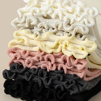 Stack of colorful scrunchies in black, pink, yellow, and white on a beige background