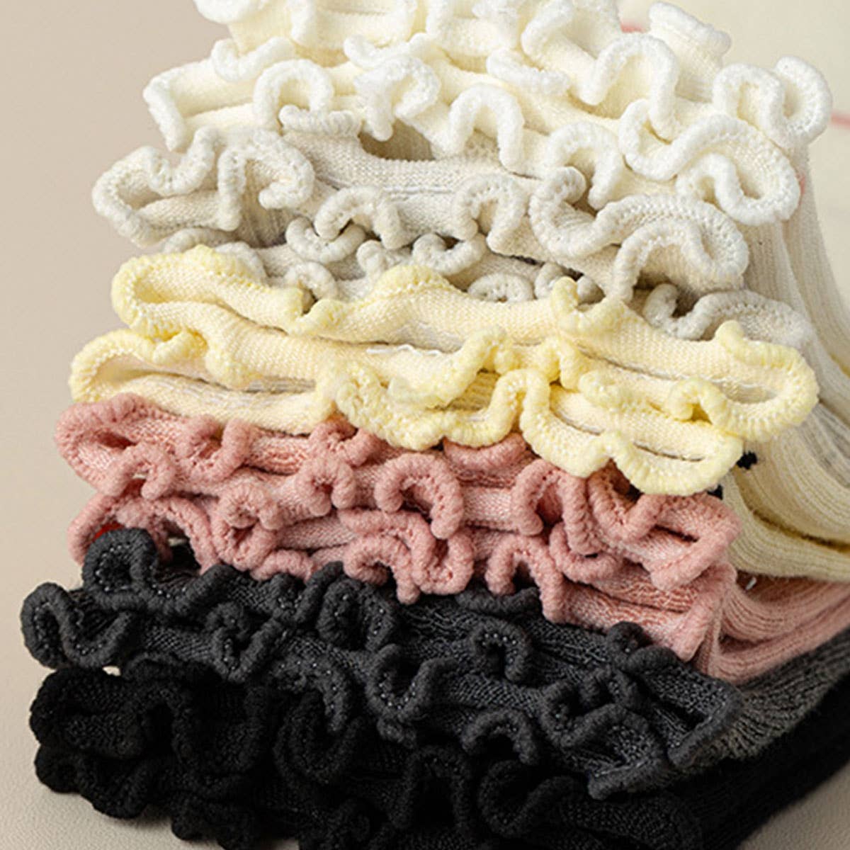 Stack of colorful scrunchies in black, pink, yellow, and white on a beige background